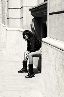 A fashionable woman wearing bold boots and patterned pants sits against a historic building
