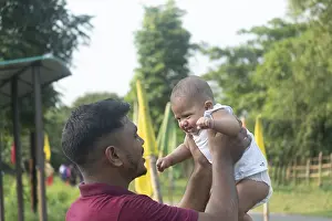 A father holds his baby, engaging in eye contact in a sunny outdoor setting-Dhaka