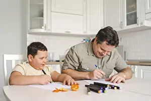A father and son enjoy drawing together at the kitchen table