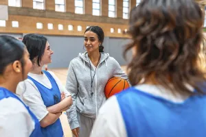 Female basketball coach holding a ball and engaging with her team during an intense training session in the gym