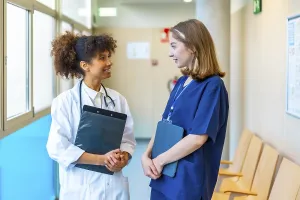 Female doctor and nurse engaging in a friendly conversation while reviewing medical records in a bustling hospital