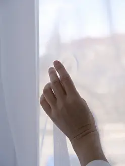 Female hand against the background of a window curtained with transparent fabric