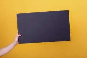 Female hand holding a blank black sheet poster for copy-space and mockup on a yellow background