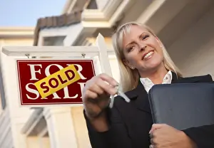 Female real estate agent with keys in front of sold sign and beautiful house