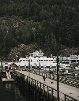 Ferry moored at a wooden pier with a dense forest and mountainous backdrop in Horseshoe Bay