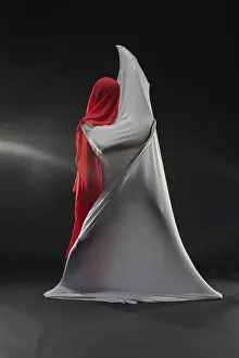 A figure in striking red fabric emerges from elegant draped materials