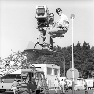 Filming in 1963. A cinematographer and his assistant sit on a moving platform during the filming of a commercial for the petrol company Esso. With a lens in front of one eye, the cinematographer makes a measurement of the light