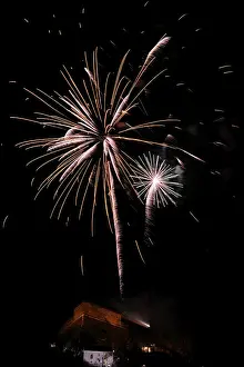 Fireworks light up the night sky above a building with glowing sparks