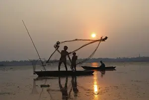 Fishermen in boat throwing net in silhouette