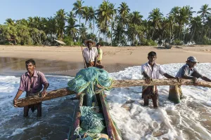 Fishermen at work, fishermen pushing fishing boat from sandy beach into the sea