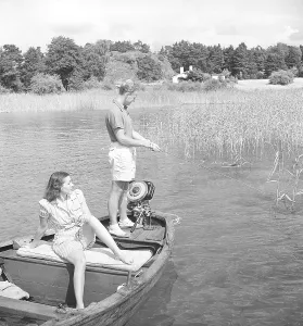 Fishing in the 1940s. A man is fishing from the boat and his girlfriend is enjoying the sun while waiting for him to catch a fish. The outboard motor is made by swedish manufacturer Penta