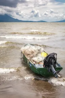A fishing boat on the shore of a lake with volcanoes in the background