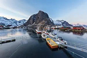 A fishing harbor with boats docked and mountain in the background at dawn