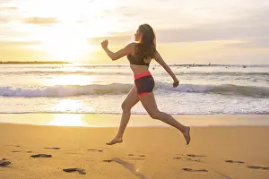 Fit woman running along a sandy beach during sunset