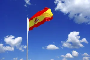 The flag of Spain flutters in the wind in a blue sky with white clouds