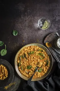Flat lay composition of hearty vegan chickpea curry soup bowl and glass of lime water on black background