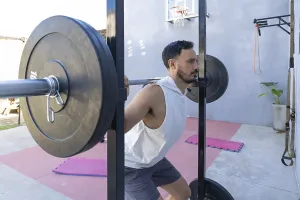 Focused male athlete lifting weights and performing squats in a home gym