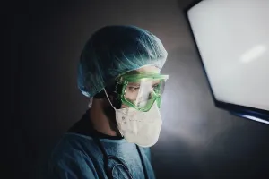 A focused medical professional in protective gear looking at a screen