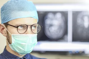 A focused surgeon wearing glasses and a mask