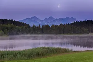 Foggy lake at dawn with visible mountains and forests