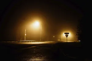 Foggy night street with glowing streetlights casting yellow light on a dark and quiet road