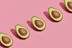 Food design. Top view of colorful fruit pattern of fresh cutted avocado halves with pits inside on coral pink pastel