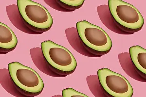 Food design. Top view of colorful fruit pattern of fresh cutted avocado halves with pits inside on coral pink pastel