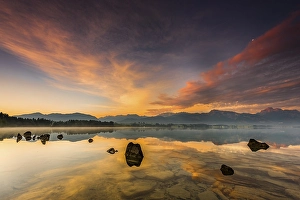 Forggensee with reflection of the cloudy sky and the Allgaeuer mountains in the background at sunrise