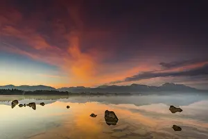 Forggensee with reflection of the cloudy sky and the Allgaeuer mountains in the background at sunrise