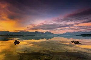 Forggensee with reflection of the cloudy sky and the Allgaeuer mountains in the background at sunrise