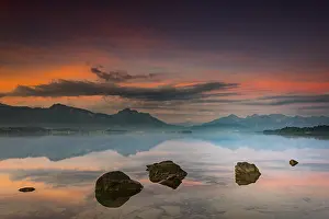 Forggensee with reflection of the cloudy sky and the Allgaeuer mountains in the background at sunrise