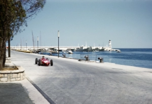 Formula One race at the 1961 Monaco Grand Prix, Richie Ginther in a shark-nosed Ferrari 156 F1 approaching a tobacco kiosk
