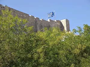 Fortress with Greek flag surrounded by green trees under a clear blue sky