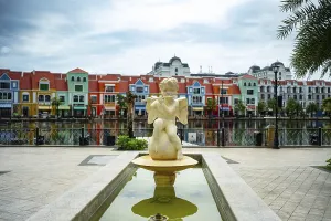 A fountain with a sculpture and a backdrop of colorful buildings reflected in the water