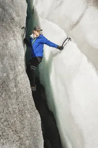 A free climber without insurance with two ice axes rises from a crack in the glacier