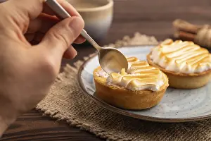 French lemon tart with meringue with hand on brown wooden background