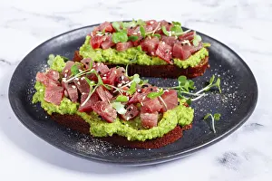 Fresh tuna tartare on avocado spread toast with microgreens served on a black plate