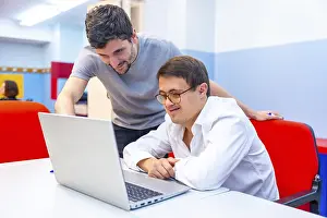 Friendly adult male teacher helping a man with down syndrome during computing class