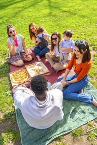 Friends and their babies are sharing pizza and drinks during a cheerful picnic in a park