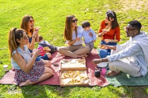 Friends and family sharing pizza and drinks at a sunny park picnic