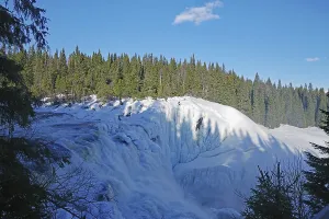 A frozen waterfall in a winter landscape with forest and clear sky