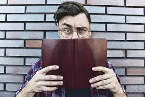 Funny face. Young hipster guy wearing eyeglasses with picked up one browe looking at camera