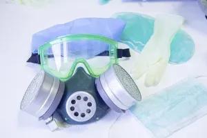 Gas mask with goggles and sterile gloves arranged on white background