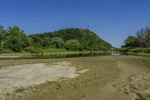 A gentle river flowing by a wooded hill with a clear sky and sunny weather in the background