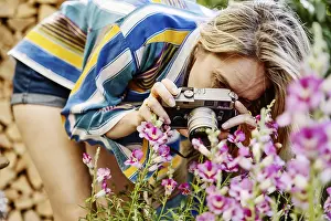 Germany, young woman photographing blooming flowers in the garden