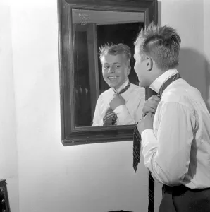 Getting dressed in the 1950s. A young man in front of the mirror knots his necktie