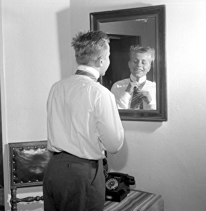 Getting dressed in the 1950s. A young man in front of the mirror knots his necktie