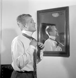 Getting dressed in the 1950s. A young man in front of the mirror knots his necktie