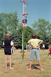 Girl climbing maypole, boys waiting