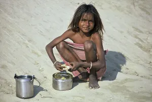 Girl at mealtime, squatting in the sand